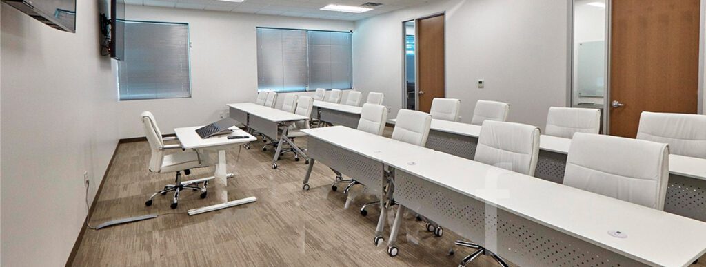Modern training or conference room with white ergonomic chairs, long white tables, and a wall-mounted TV in a professional office setting