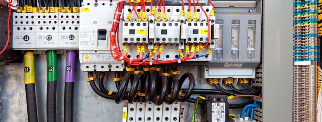 Close-up of an industrial electrical panel with labeled circuit breakers, wiring, and fuses for power distribution and control.